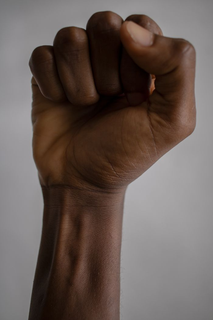 Isolated crop anonymous ethnic person demonstrating inner side of fist raised against gray background